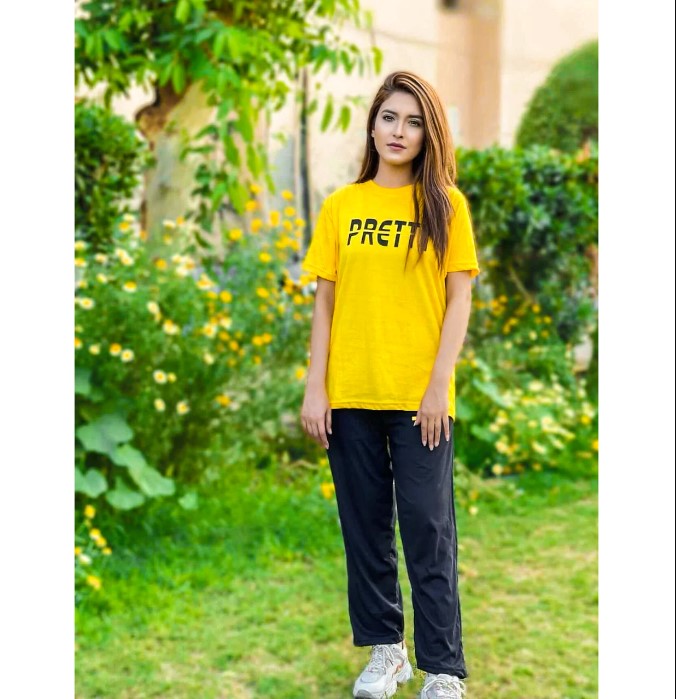 a woman in a yellow shirt standing in a garden 